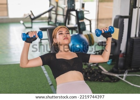 A young asian woman does a set of incline dumbbell presses at the gym. Chest and upper body toning exercise. Royalty-Free Stock Photo #2219744397