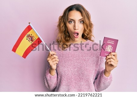 Young caucasian woman holding spain flag and passport afraid and shocked with surprise and amazed expression, fear and excited face. 