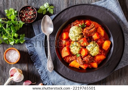 Beef Stew with Dumplings and vegetables in rich tomato and stock based gravy in black , flat lay