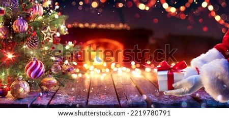 Santa Claus Give Present Under Christmas Tree - Gift Box and Ornament In Interior Home With Abstract Defocused Lights At Night