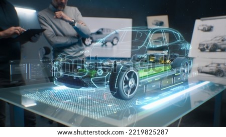 Car design engineers using holographic app in digital tablet. Develop modern innovative high-tech cutting edge eco-friendly electric car with sustainable standards. They test the aerodynamic qualities Royalty-Free Stock Photo #2219825287