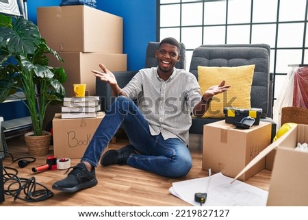 African american man sitting on the floor at new home smiling cheerful offering hands giving assistance and acceptance. 