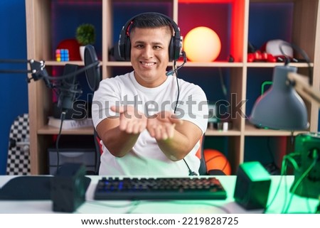 Young hispanic man playing video games smiling with hands palms together receiving or giving gesture. hold and protection 