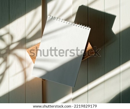 The shadow of a home plant falls on a blank sheet of an open notebook. A simple concept of planning things, learning, making lists, keeping a diary. Flat lay. Top view. Copy space.