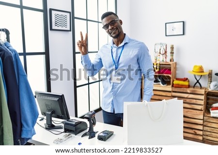Young african man working as manager at retail boutique smiling looking to the camera showing fingers doing victory sign. number two. 