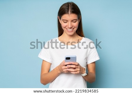 Girl wearing smart watch synchronized with her smartphone, texting message to her boyfriend using online chat. Young woman searching love in mobile dating app isolated on blue background