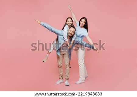 Full body young parents mom dad with child kid daughter teen girl in blue clothes give piggyback ride to kid sit on back stretch arms isolated on plain pastel light pink background Family day concept