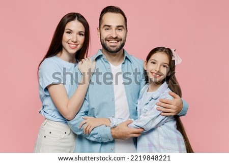 Young smiling parents mom dad with child kid daughter teen girl in blue clothes hugging each other look camera isolated on plain pastel light pink background. Family day parenthood childhood concept