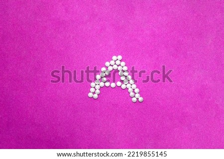 Letter A made of pills on pink velvet paper