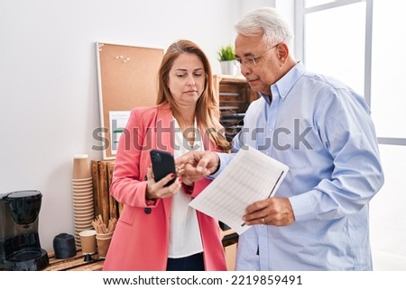 Middle age man and woman business workers using smartphone reading document at office