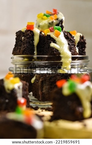 Close up picture of brownies cake in glass jar with cheese and fruit glaze as topping. Selective focus, bokeh foreground