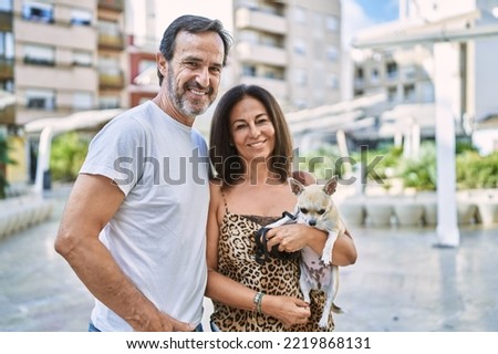 Middle age man and woman couple holding chihuahua hugging each other at street