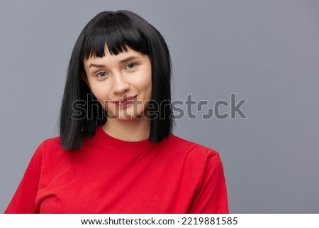 horizontal photo of a beautiful woman with short black hair looking pleasantly into the camera standing on a gray background in a red T-shirt