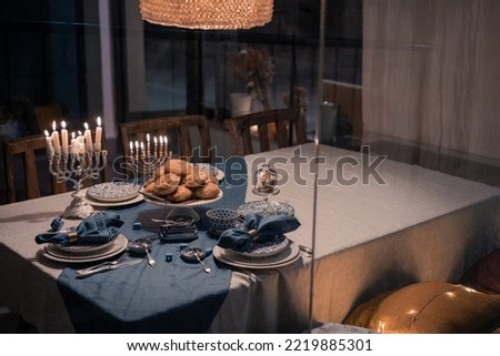 Food for Hanukkah celebration: Menorah Candles on wooden table, sufganiyot cake and table setting, jewish symbol centerpieces, white and blue. holiday Israel hebrew traditional family celebration Royalty-Free Stock Photo #2219885301