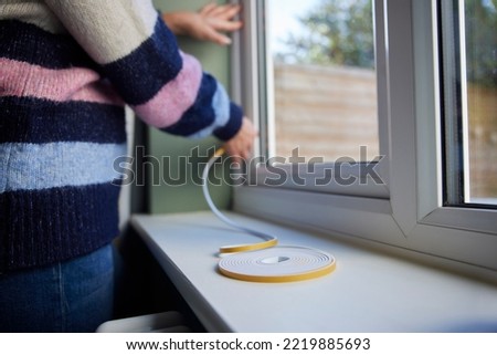 Woman Saving Enegy Insulating Home Putting Draught Excluder Tape On Window Royalty-Free Stock Photo #2219885693