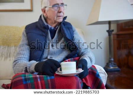 Senior Man Wearing Extra Clothes With Hot Drink Trying To Keep Warm At Home In Energy Crisis Royalty-Free Stock Photo #2219885703