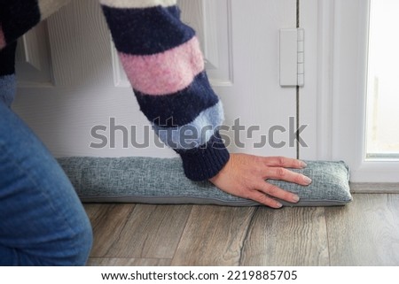Close Up Of Woman Saving Enegy Insulating Home Putting Draught Excluder Against Front Door Royalty-Free Stock Photo #2219885705