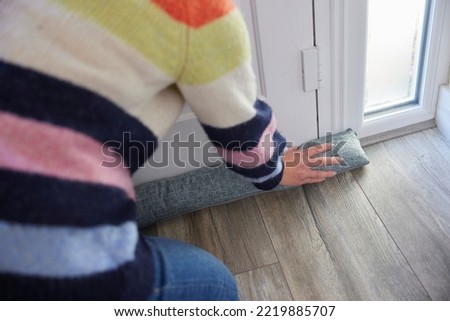 Close Up Of Woman Saving Enegy Insulating Home Putting Draught Excluder Against Front Door Royalty-Free Stock Photo #2219885707