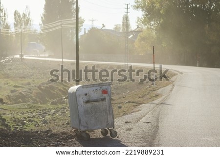 A garbage container standing by the roadside in Sunny Foggy weather.