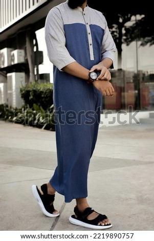 young Asian man wearing thobe with modern design against blurred restaurant. modern Moslem wear. common arabian man's outfit Royalty-Free Stock Photo #2219890757