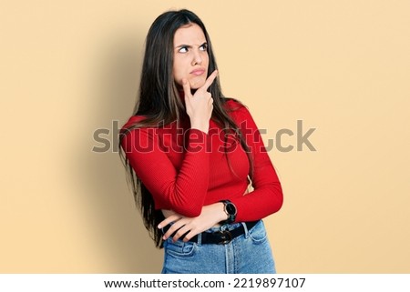 Young brunette teenager wearing red turtleneck sweater thinking worried about a question, concerned and nervous with hand on chin 