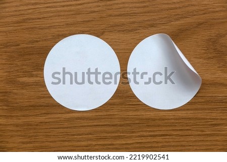 Blank white round stickers straightened and with folded corner on wooden background.