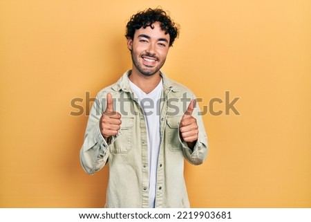 Young hispanic man wearing casual clothes success sign doing positive gesture with hand, thumbs up smiling and happy. cheerful expression and winner gesture. 