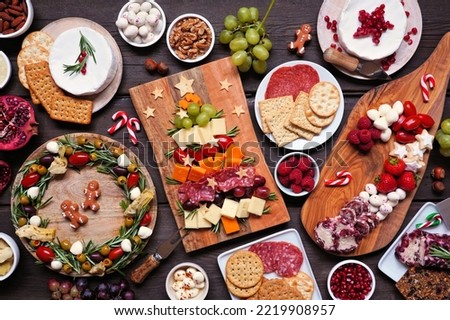 Christmas charcuterie table scene against a dark wood background. Assortment of cheese and meat appetizers. Christmas tree, wreath and candy cane arrangements. Royalty-Free Stock Photo #2219908957