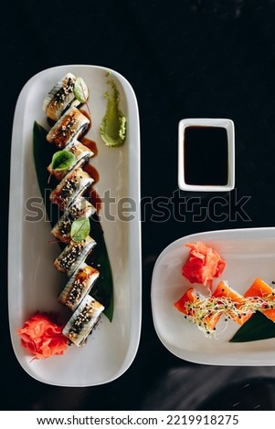 Sushi with black rice and red fish and cucumber on a white plate decorated with greens.