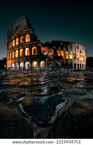Portrait picture of the Roman Colosseum at night with wet cobblestones reflecting the illuminated ancient arena Royalty-Free Stock Photo #2219934751