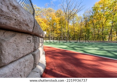 Interesting green and red outdoor basketball court at school playground.  Court includes retaining walls and black vinyl coated chain link fence.	