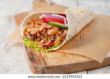 doner donair kebab wrap with spicy meat, lettuce, tomato, red onion. Served on wooden cutting board. Copy space for text or logos.	 Royalty-Free Stock Photo #2219943323