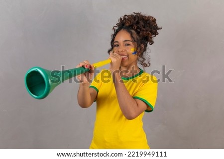 Young brazilian cheerleader with a vuvuzela on grey background celebrating