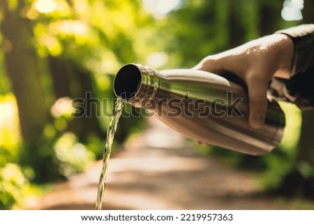 Close-up of Unrecognizable female hand holding Water bottle. Pouring clean water Reusable steel thermo water bottle in park. Sustainable lifestyle. Plastic free zero waste free living. Go green Woman