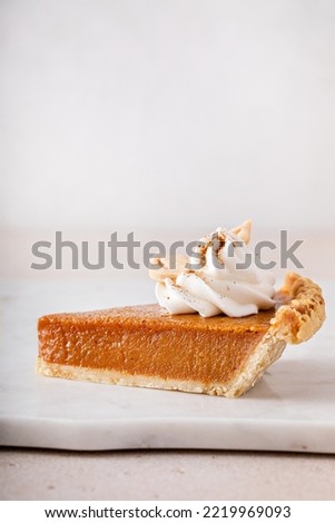 Pumpkin pie slice topped with whipped cream on a marble board, minimalistic look with copy space