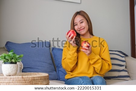 Portrait image of a young woman holding and eating an apple at home