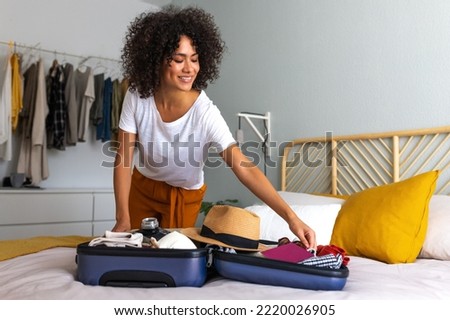 Happy African American young woman packing suitcase at home. Preparing for summer holidays abroad. Royalty-Free Stock Photo #2220026905