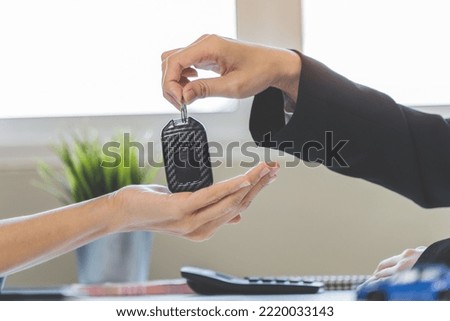 Car rental service concept. Close up view Hand of agent giving car key to customer after signed rental contract form.