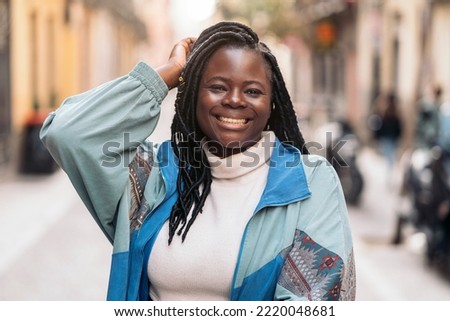 Happy and young african woman with cool braids smiling and looking at camera. She is in the street.