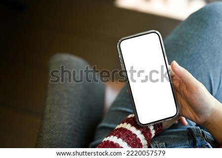 A smartphone white screen mockup is in a woman's hand over her laps. mobile application banner mockup. cropped image