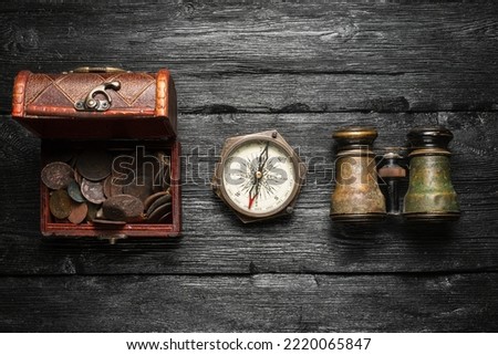 Treasure chest with coins, compass and binoculars on the old wooden table flat lay background. Pirate concept background. 