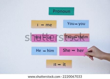 Closeup hand holds pink paper card with word "She-her" on it. .  Concept : English grammar teaching by using word card Teaching aid, Education materials. Pronouns                                      