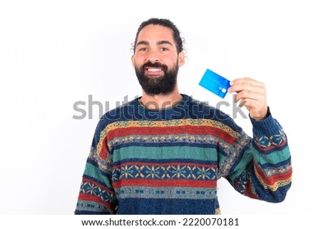 Photo of happy cheerful smiling positive young hispanic bearded man wearing knitted sweater over white background recommend credit card