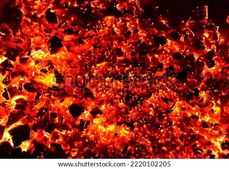 There are red and orange smouldering coals of the campfire in the dark. Background picture.