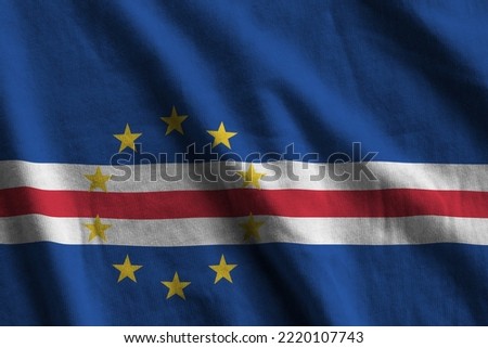 Cabo verde flag with big folds waving close up under the studio light indoors. The official symbols and colors in fabric banner