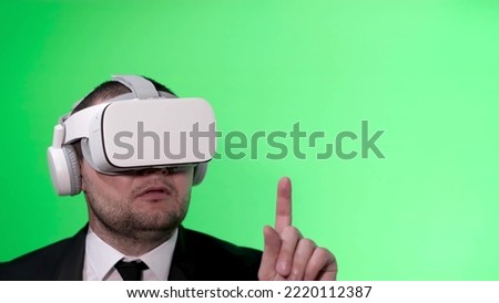 A man in a black suit uses virtual reality goggles. VR. Green background. The office worker