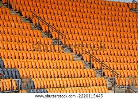 rows of vacant orange fold down seats at a sports stadium