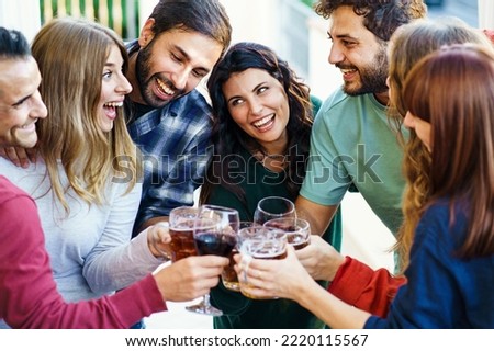 Friends cheering together toasting beer and wine standing on the balcony - - Friendship concept with young people having fun gathering together at home party - Focus on the brunette in the center