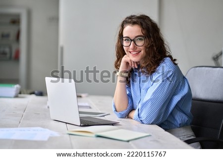 Young happy business woman company employee sitting at desk working on laptop. Smiling female professional entrepreneur worker using computer in corporate modern office looking at camera. Portrait. Royalty-Free Stock Photo #2220115767