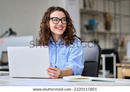Young happy business woman company employee, marketing manager sitting at desk working on laptop. Pretty female professional worker using computer in corporate modern office looking away and smiling. Royalty-Free Stock Photo #2220115801